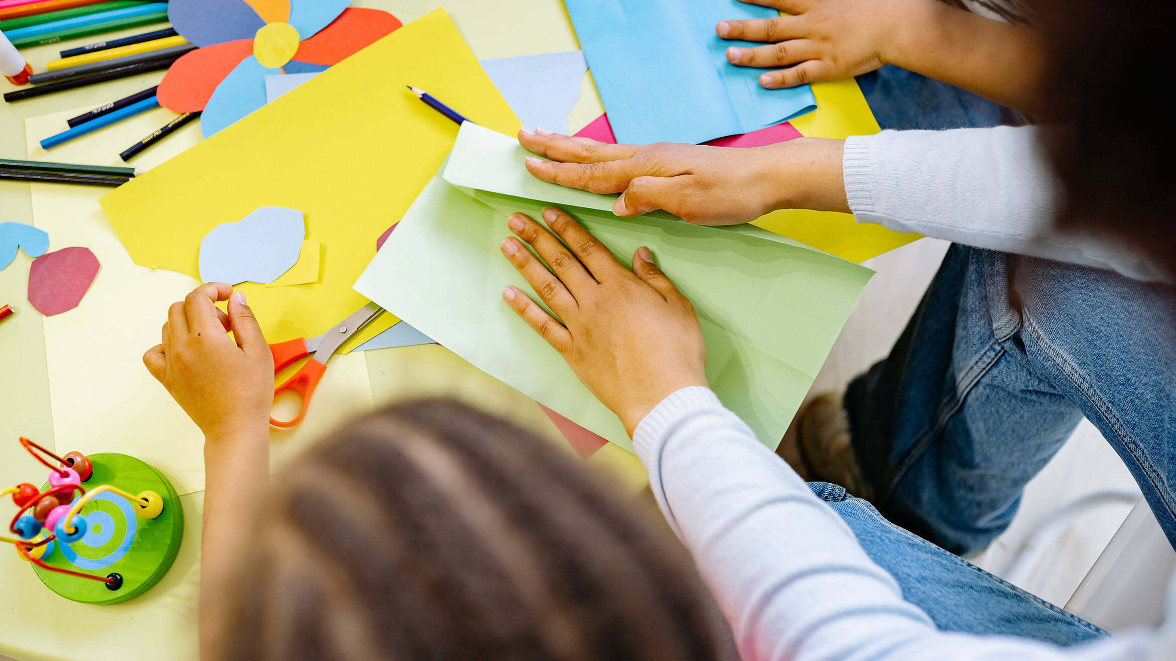 Top down view of children using arts and crafts materials with an adult helping