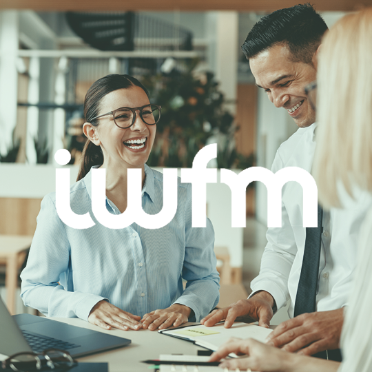 A smiling smartly dressed woman in an office environment having a meeting with a man and another woman