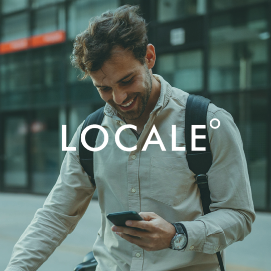 A smiling man wearing a shirt and a backpack using his phone